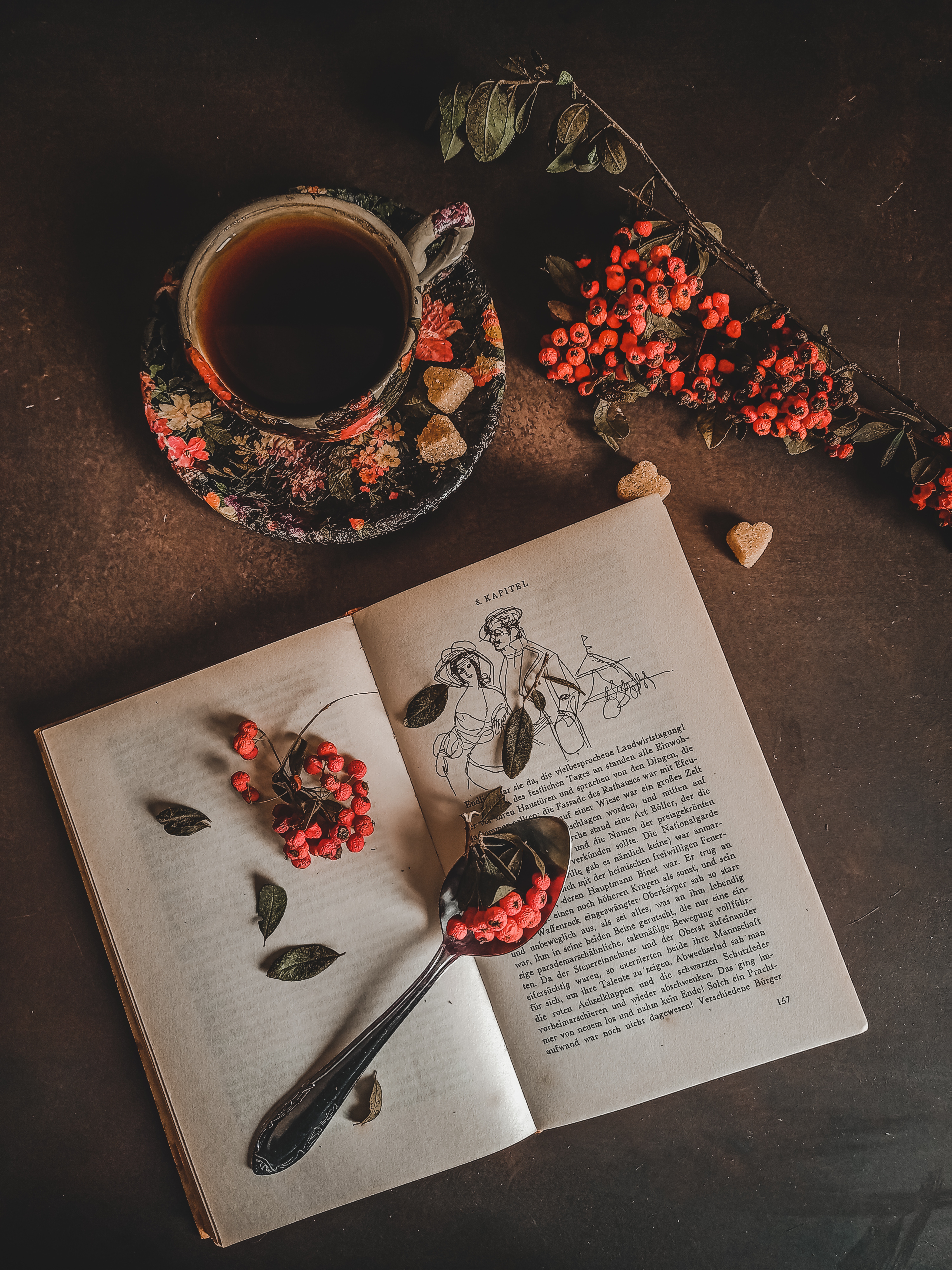 Elaborate Daydreams shot of floral coffee cup beside an open book, invoking a cozy and pretty aesthetic